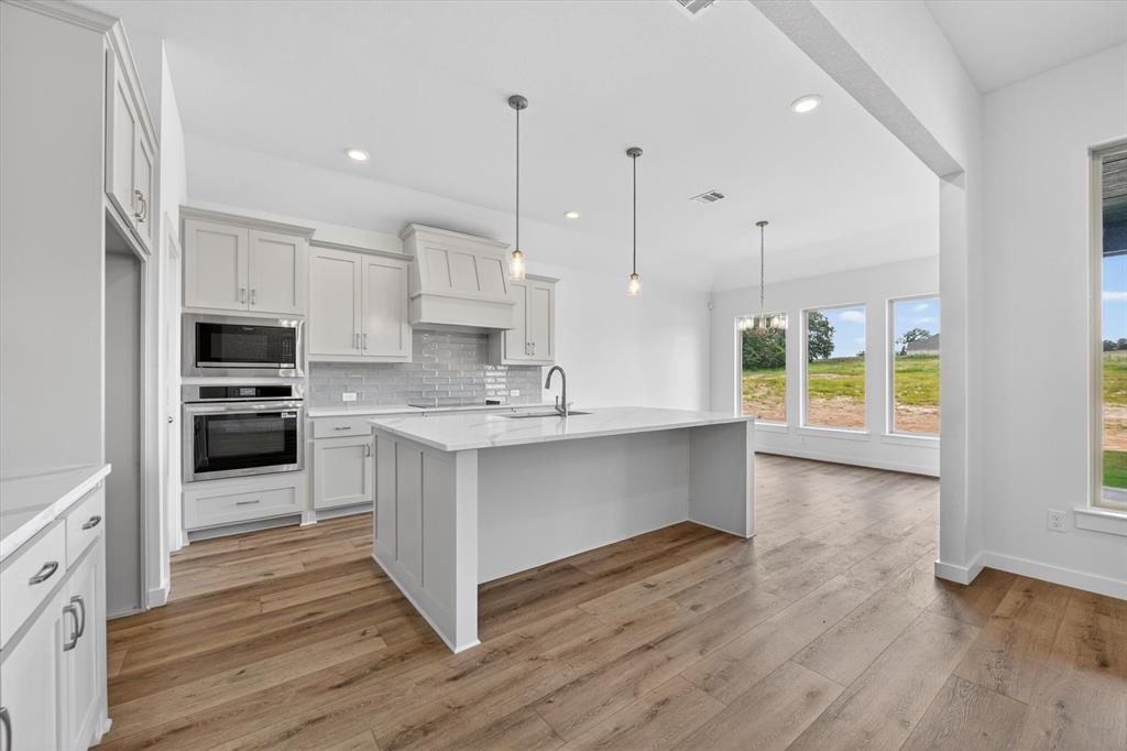 416 McAlpine Drive Springtown, TX 76082 - Photo 16 of 40 Modern kitchen with wood-finish flooring, light gray cabinetry, stainless steel built-in appliances, a quartz-finish island, and pendant lighting