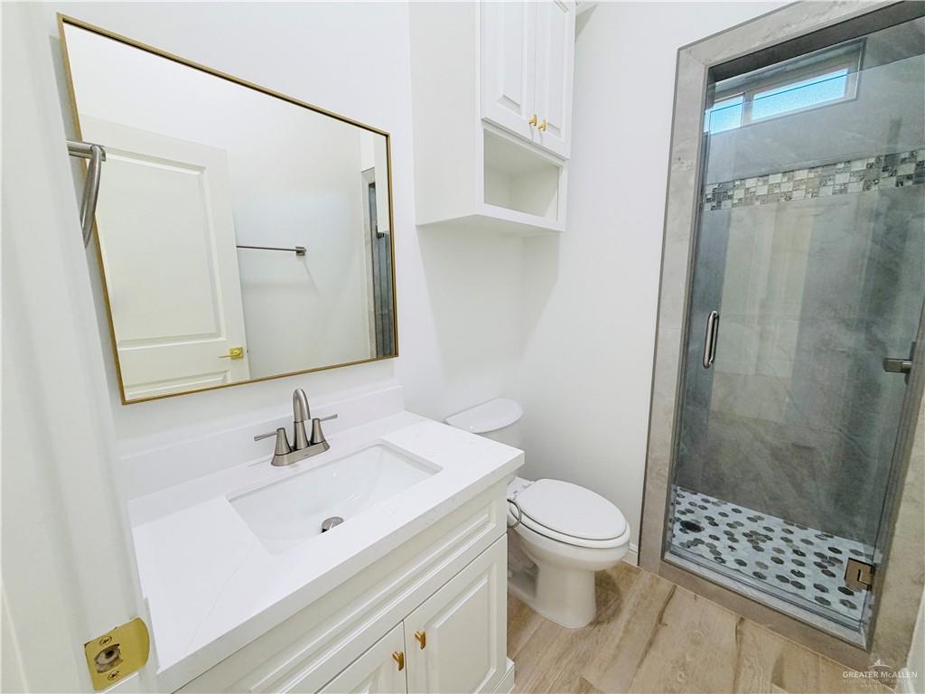 807 Ramirez Street Mission, TX 78573 - Photo 11 of 16 Modern bathroom featuring a white vanity with gold hardware and rectangular sink, quartz countertop, framed mirror with brass trim, and a walk-in shower with glass enclosure and mosaic tile flooring