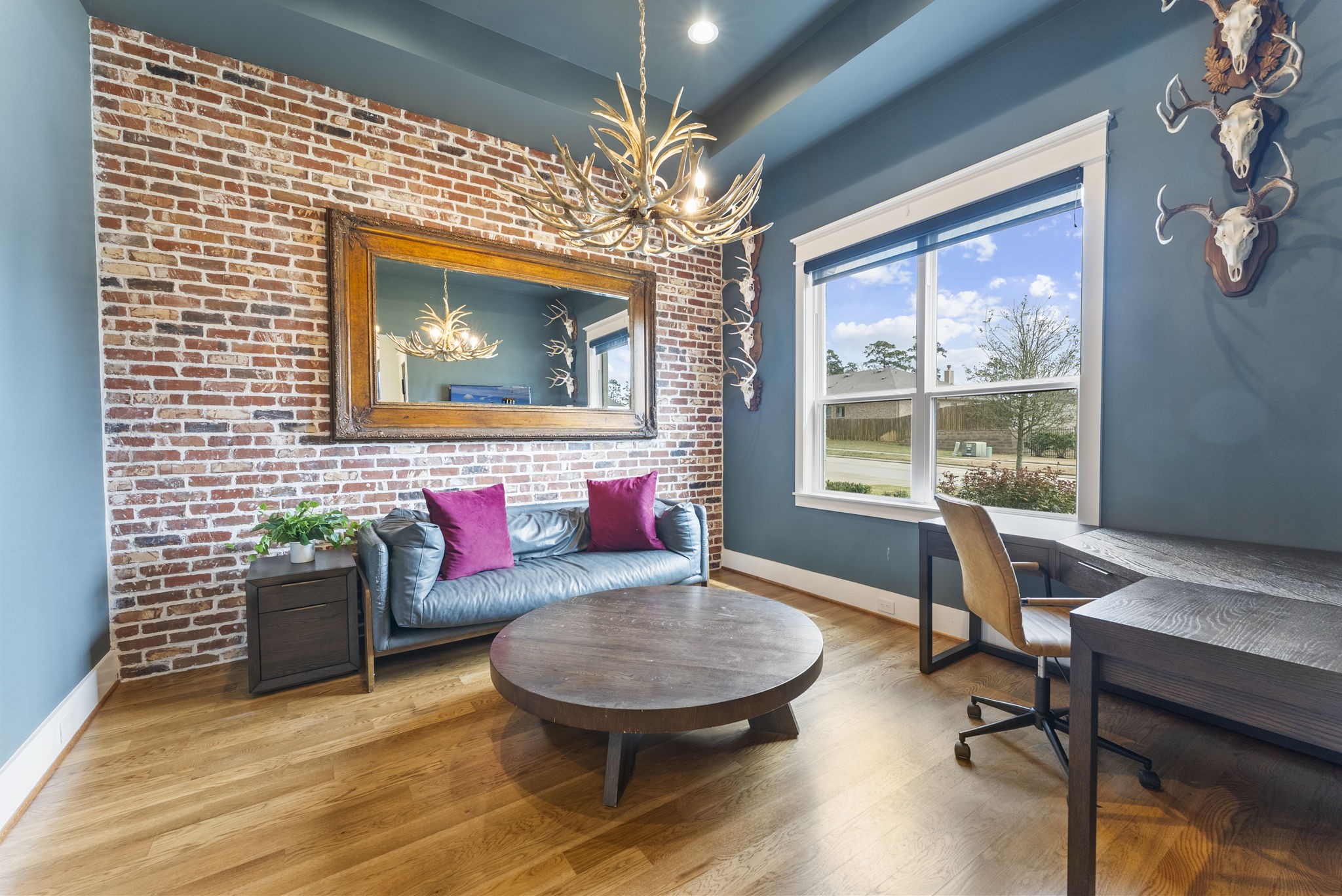 14019 Beartooth Bend Trail Conroe, TX 77384 - Photo 4 of 28 Flexible dining or study area showcasing gleaming hardwood floors, abundant natural light from oversized windows, a sophisticated tray ceiling, a bold brick accent wall, and a dramatic antler chandelier.
