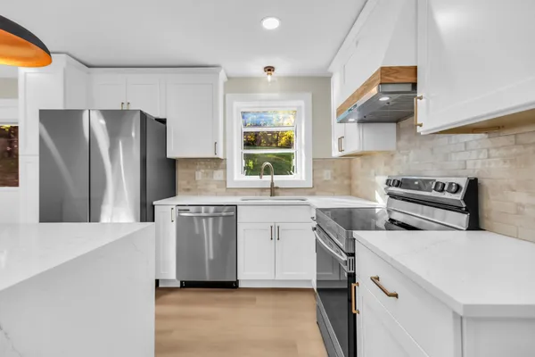 a kitchen with stainless steel appliances a refrigerator a sink dishwasher a stove and white cabinets with wooden floor