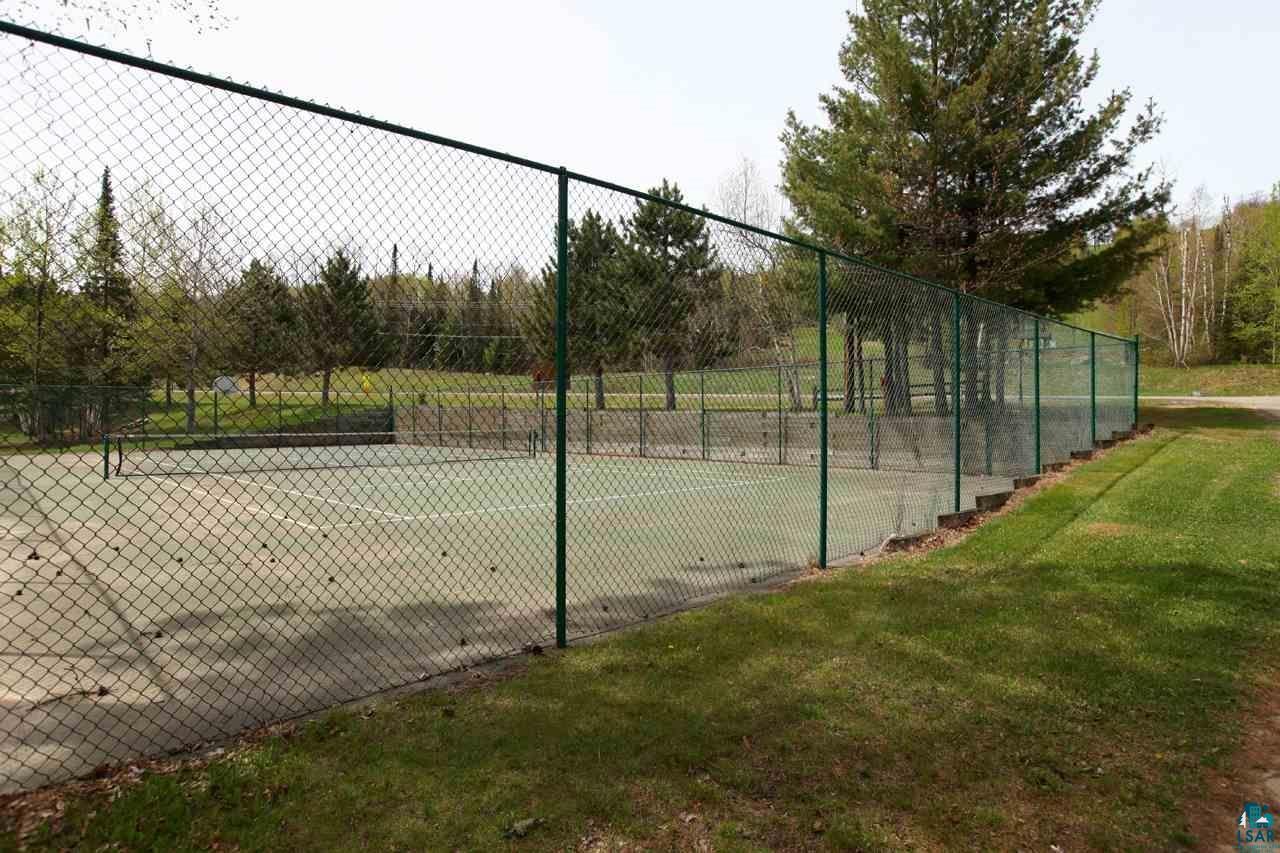 6266 Giants Ridge Road, Unit 704 Biwabik, MN 55705 - Photo 23 of 23 Outdoor tennis court featuring a chain-link fence, green surface, and surrounding grassy areas with mature trees
