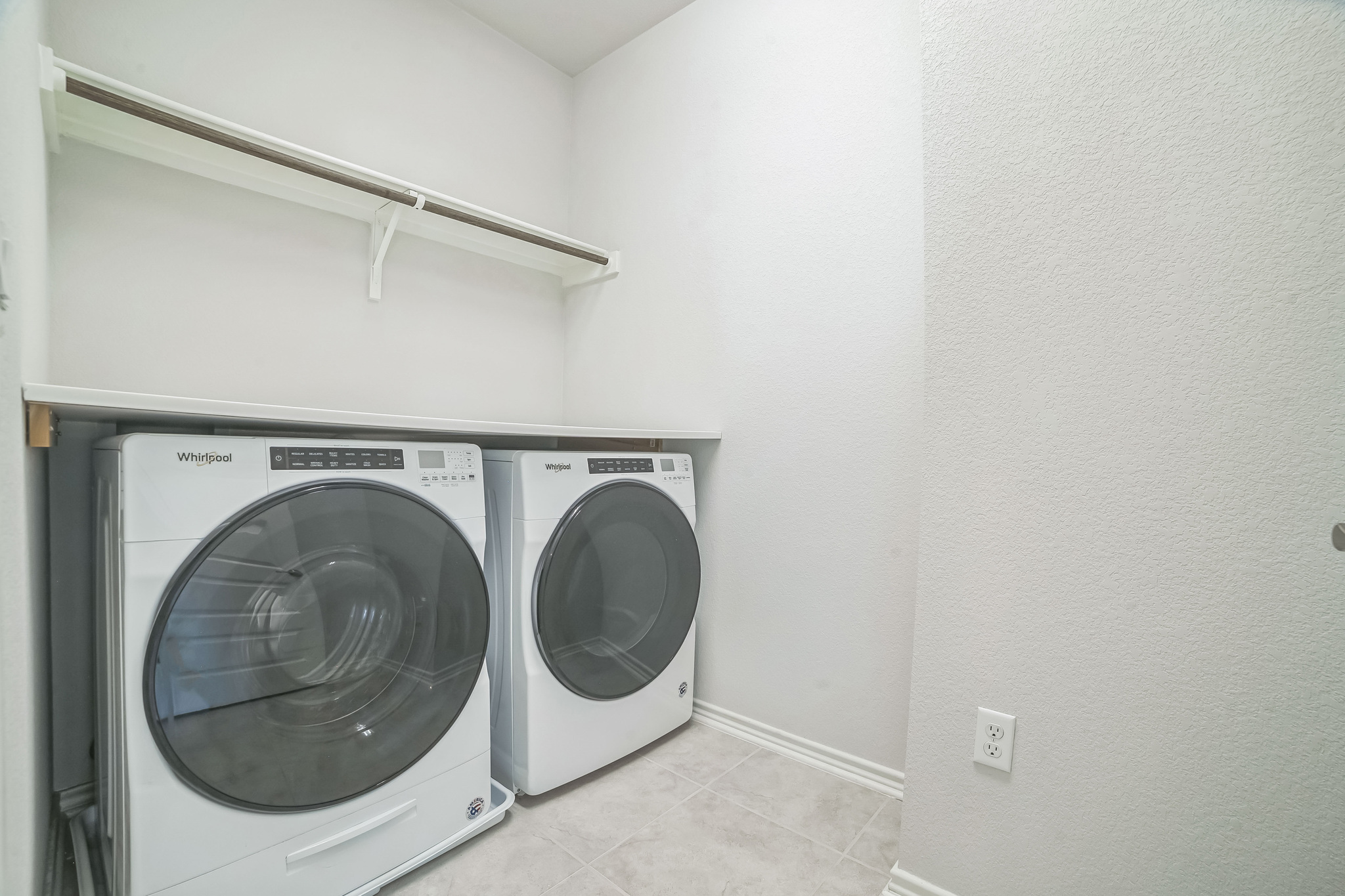 14300 McCoy Loop, Unit 21 Austin, TX 78717 - Photo 21 of 40 This utility area features a full-size washer and dryer, a shelf, and a clothes hanging rod, complemented by light-colored walls and tiled flooring