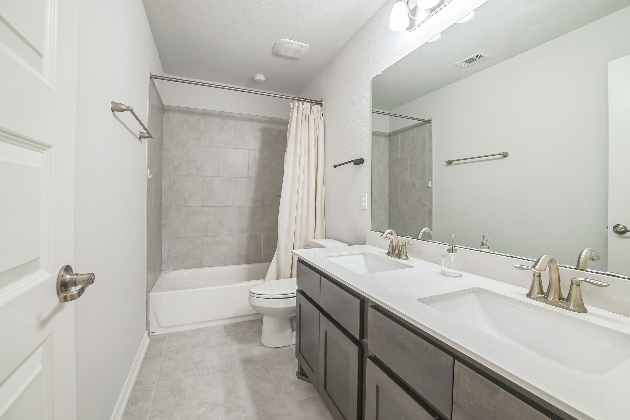 14300 McCoy Loop, Unit 21 Austin, TX 78717 - Photo 30 of 40 Bathroom featuring a double vanity with white countertops and brushed nickel faucets, a large mirror, and a combination bathtub and shower with tiled walls