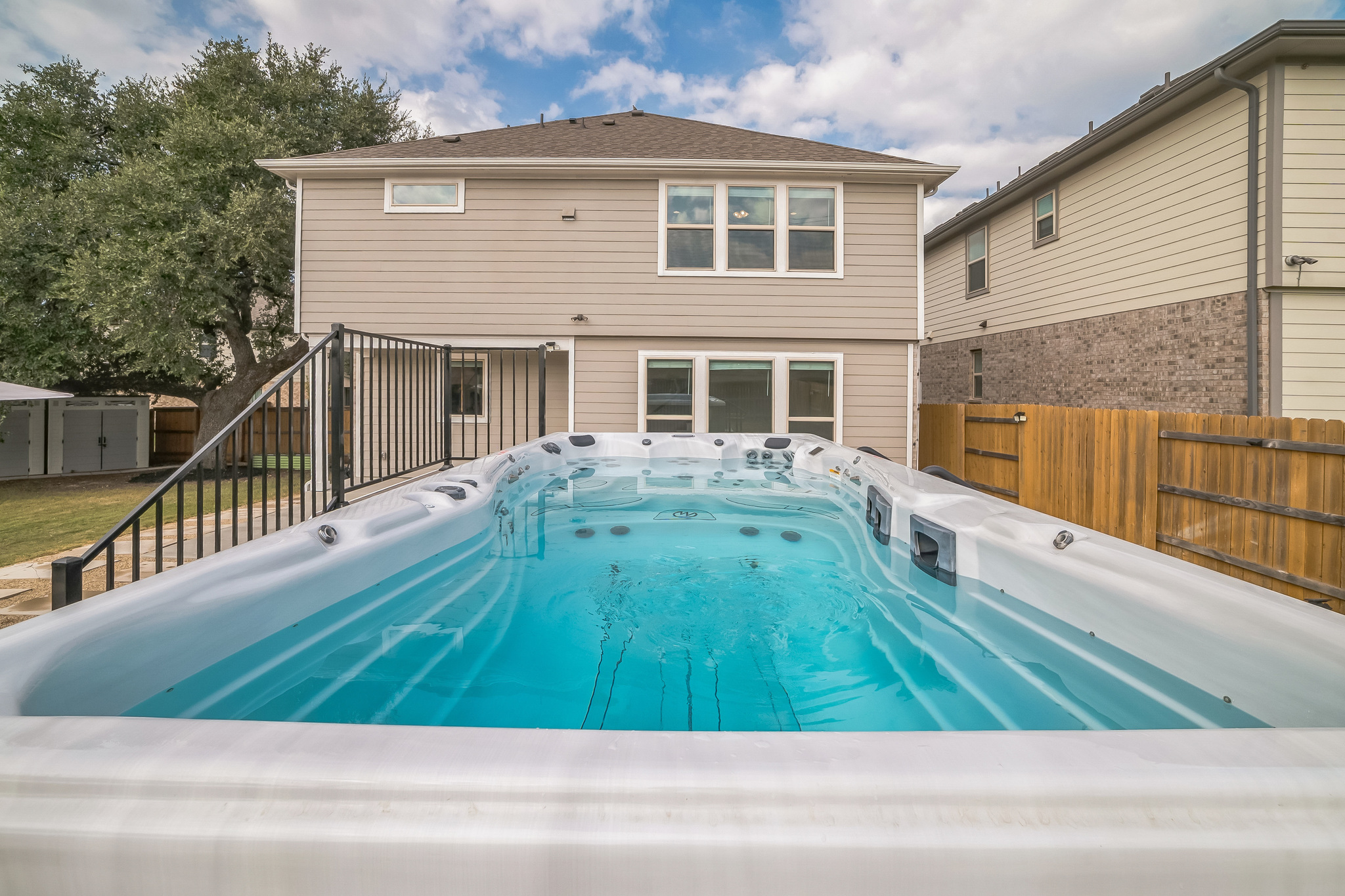 14300 McCoy Loop, Unit 21 Austin, TX 78717 - Photo 3 of 40 The property features an extensive swim spa, a wooden fence, and a well-maintained lawn with mature trees