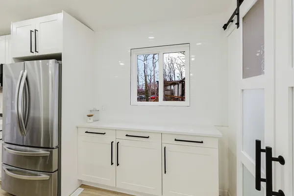 a large white kitchen with stainless steel appliances kitchen island granite countertop a couch and a view of living room