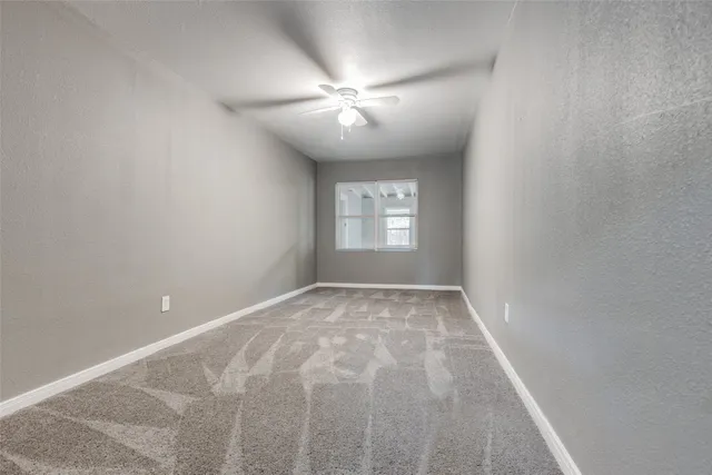 a view of an empty room with window and chandelier fan
