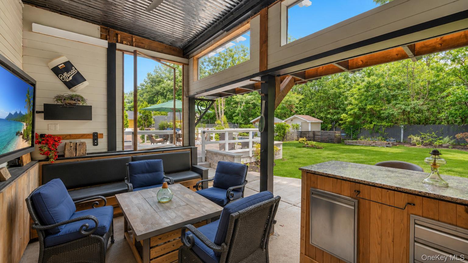 19 Joan Road Bay Shore, NY 11706 - Photo 47 of 50 Outdoor entertainment area featuring a corrugated metal roof, wood shake bar with a stone countertop, built-in media console with television, exterior wall-mounted lighting, and integrated bench seating