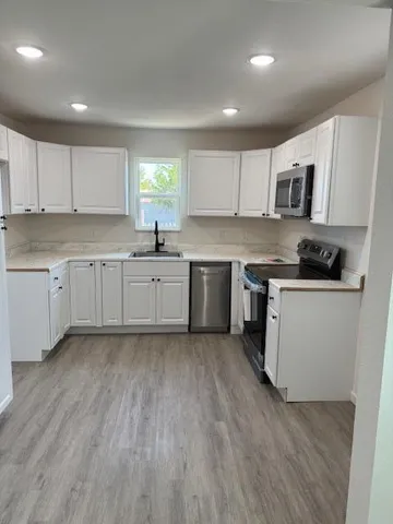 a kitchen with stainless steel appliances granite countertop a stove top oven a sink dishwasher and white cabinets with wooden floor