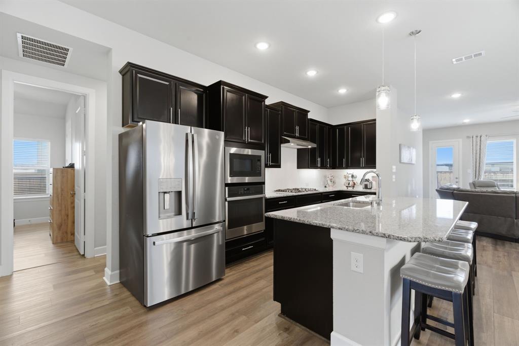 3721 Prickly Pear Road Little Elm, TX 75068 - Photo 8 of 21 Modern kitchen featuring wood-finish flooring, dark cabinetry, stainless steel appliances, a kitchen island with stone countertops, and recessed lighting
