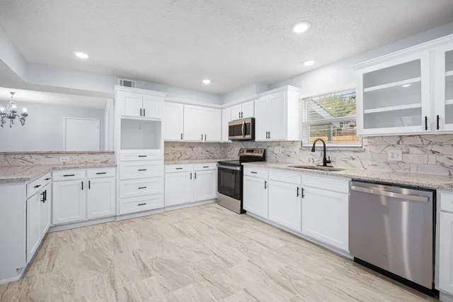 a large kitchen with stainless steel appliances granite countertop a stove a sink dishwasher and white cabinets with wooden floor