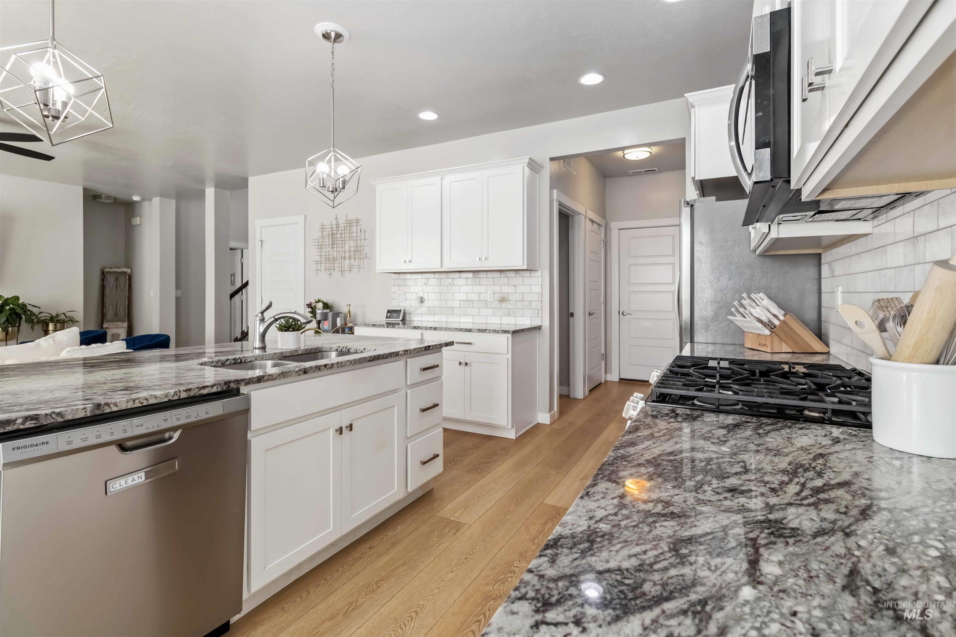 892 North Chastain Lane Eagle, ID 83616 - Photo 12 of 45 Kitchen featuring light stone counters, appliances with stainless steel finishes, white cabinets, tasteful backsplash, and light wood finished floors