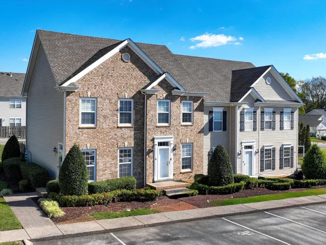 a view of a brick house with a yard plants and large tree