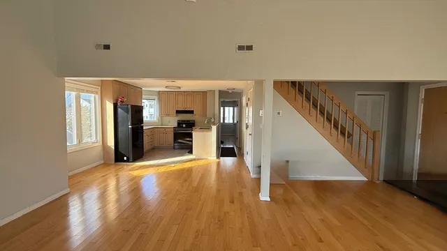 a view of an empty room with wooden floor and a kitchen