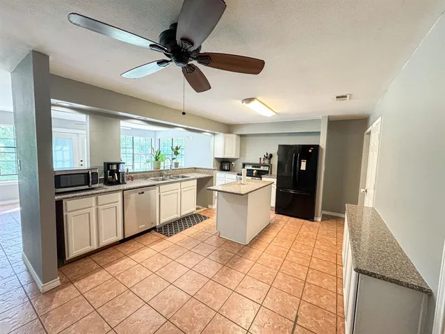 a large kitchen with a stove a sink dishwasher a refrigerator and white cabinets with wooden floor