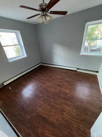 an empty room with wooden floor fan and windows