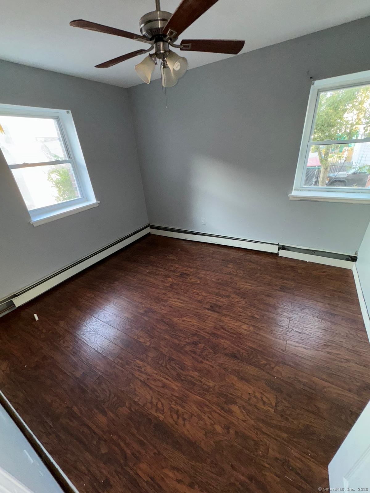 an empty room with wooden floor fan and windows