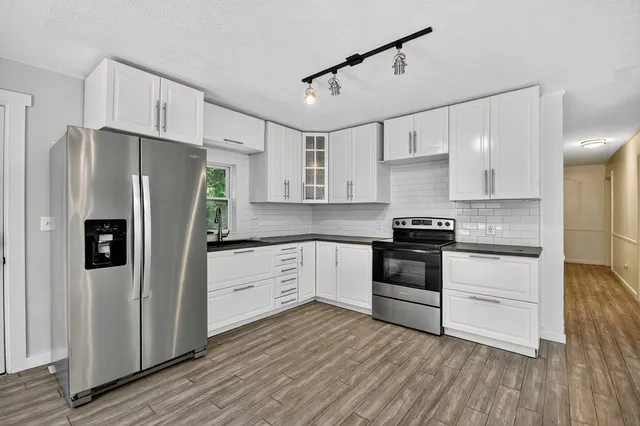 a kitchen with stainless steel appliances white cabinets wooden floor and a window
