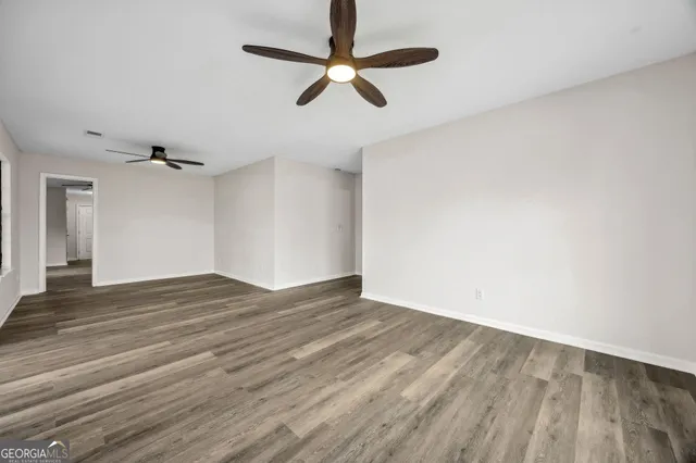 an empty room with wooden floor ceiling fan and windows