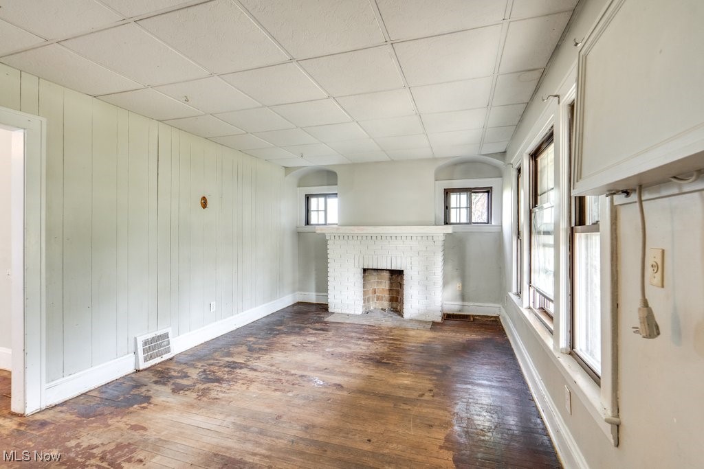 1618 Catalpa Road Cleveland, OH 44112 - Photo 10 of 33 Unfurnished living room with dark wood-style floors, a brick fireplace, a paneled ceiling, and wooden walls