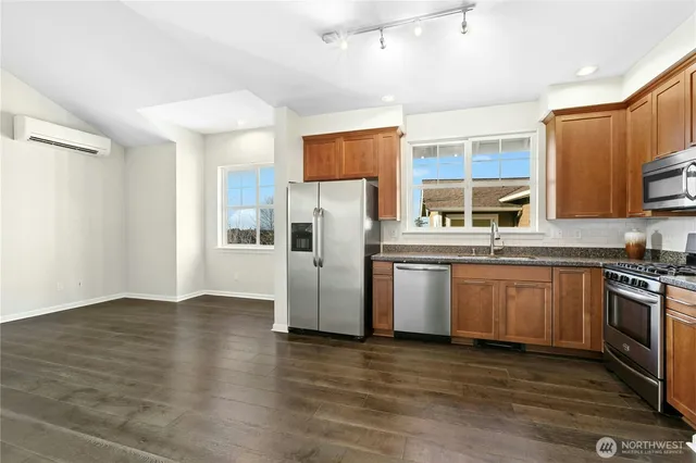 a kitchen with stainless steel appliances granite countertop a stove top oven a sink dishwasher and a refrigerator with wooden floor