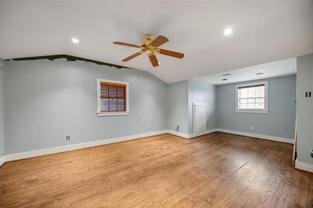 an empty room with wooden floor ceiling fan and windows