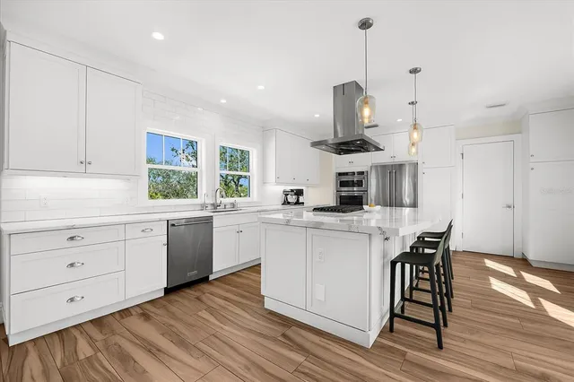 a kitchen with stainless steel appliances kitchen island granite countertop a stove a sink dishwasher and white cabinets with wooden floor