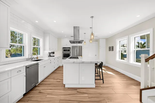 a large kitchen with stainless steel appliances kitchen island granite countertop a stove a sink a refrigerator and white cabinets with wooden floor