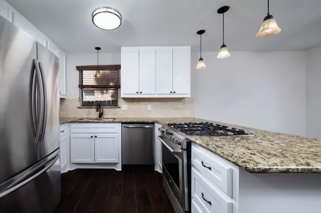 a kitchen with granite countertop a sink stainless steel appliances and white cabinets