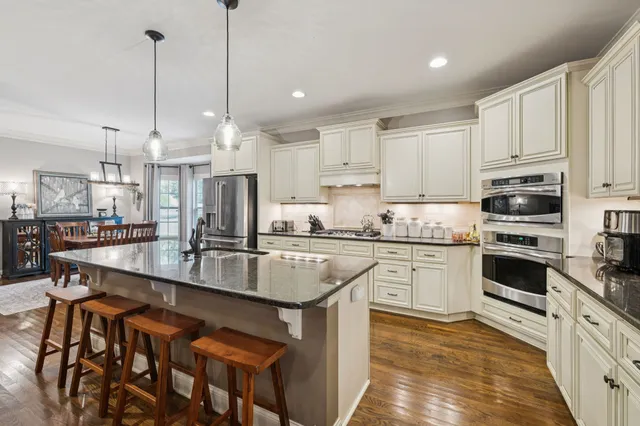 a kitchen with stainless steel appliances granite countertop a refrigerator a sink dishwasher a stove and white cabinets with wooden floor