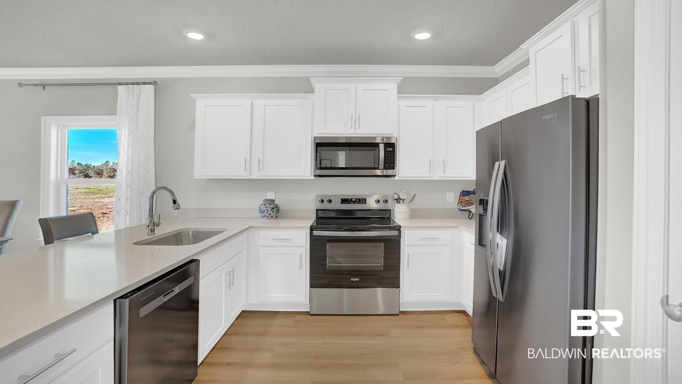 13312 Shea Circle Foley, AL 36535 - Photo 5 of 17 Modern kitchen featuring white shaker cabinetry, stainless steel appliances, light-toned countertops, a stainless steel undermount sink with a gooseneck faucet, and wood-finish flooring