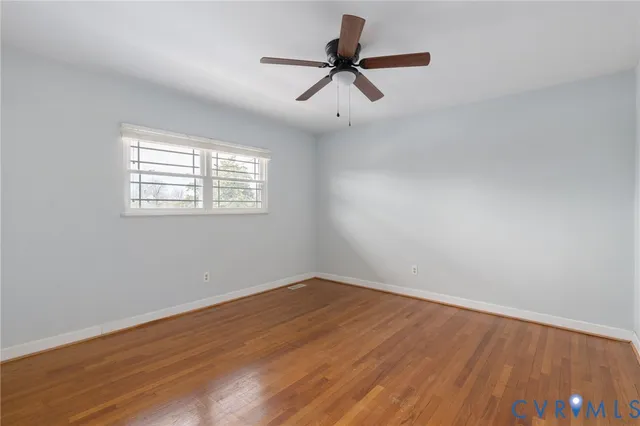 an empty room with wooden floor ceiling fan and windows