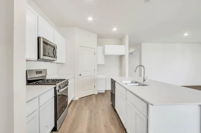 a kitchen with stainless steel appliances granite countertop a sink stove refrigerator and white cabinets with wooden floor