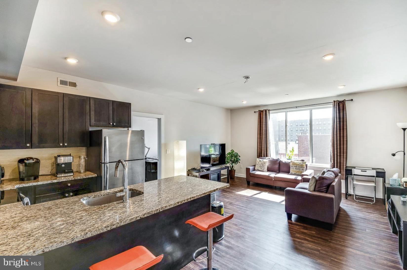 a living room with stainless steel appliances granite countertop a couch wooden floor and a refrigerator