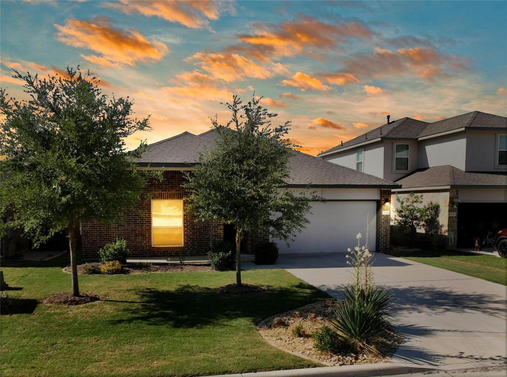 View of front of property featuring brick siding, concrete driveway, a lawn, an attached garage, and a shingled roof