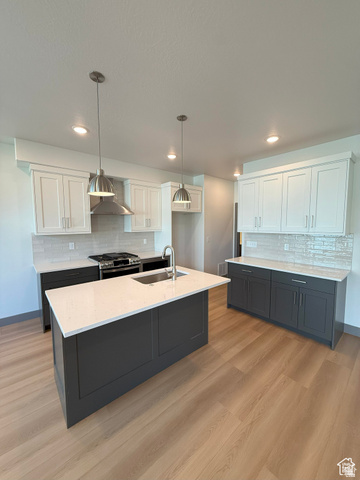 8087 South 615 East, Unit 3 Sandy, UT 84070 - Photo 6 of 23 Modern kitchen featuring a central island with an integrated sink, light-toned wood-finish flooring, two-tone cabinetry, quartz countertops, and a tiled backsplash