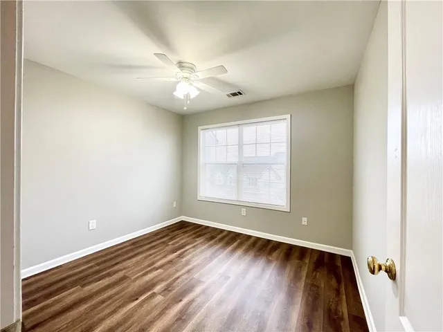 an empty room with wooden floor fan and windows