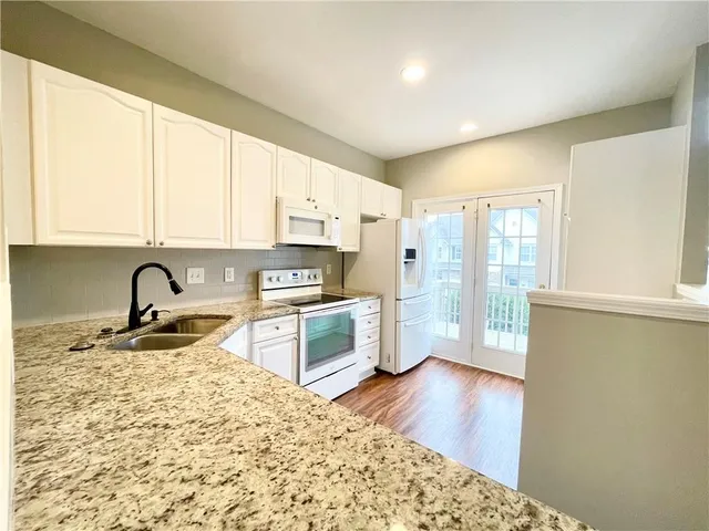 a large kitchen with granite countertop a stove a sink dishwasher a refrigerator with wooden cabinets and floor