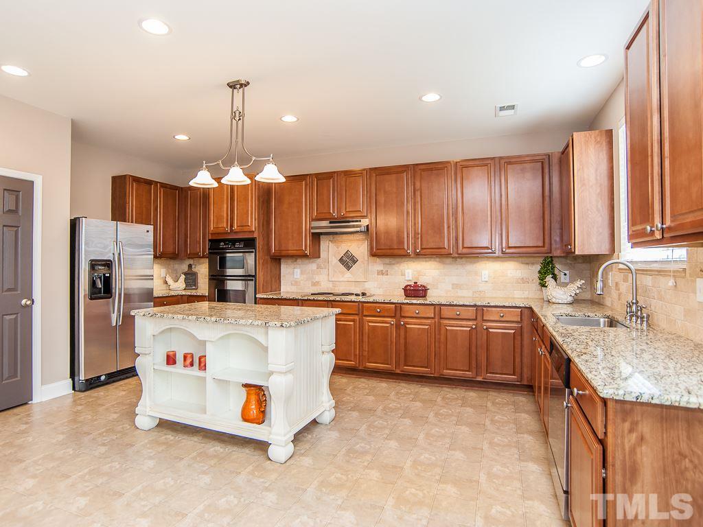 6040 Ricker Road Raleigh, NC 27610 - Photo 3 of 25 a kitchen with kitchen island granite countertop a stove a sink a oven and a refrigerator with wooden cabinets