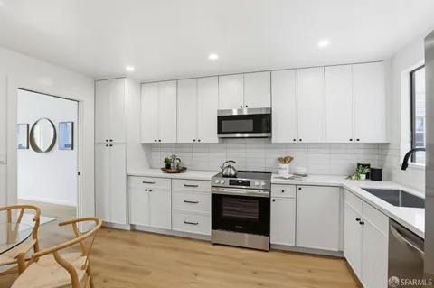 a kitchen with stainless steel appliances granite countertop a stove top oven a sink dishwasher and a refrigerator with wooden floor