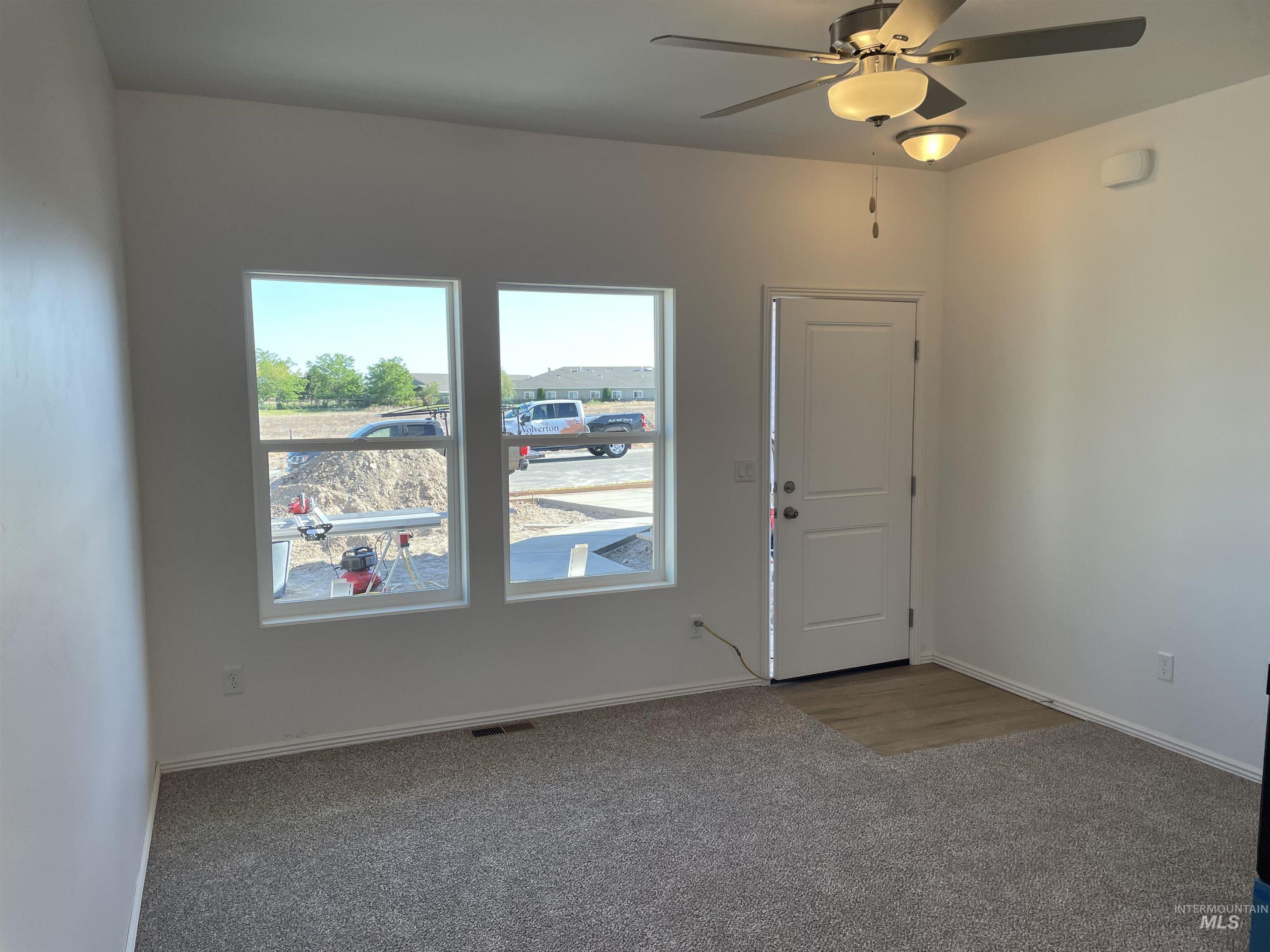 933 Roen Road Jerome, ID 83338 - Photo 4 of 13 Bright interior space featuring two large windows, neutral carpeting, a front entry door with light wood-finish flooring, and a ceiling fan with integrated lighting