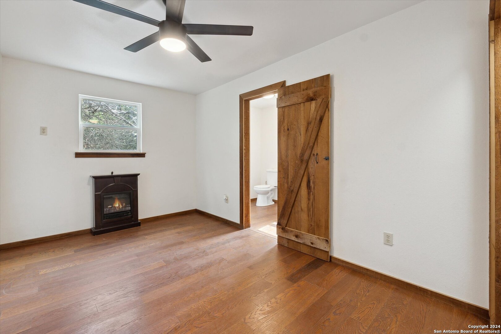 497 Black Bass Road Lakehills, TX 78063 - Photo 23 of 54 an empty room with wooden floor fireplace and windows