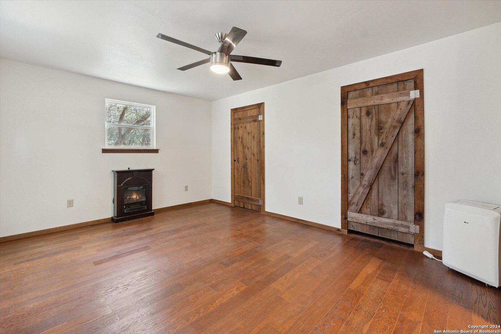 497 Black Bass Road Lakehills, TX 78063 - Photo 25 of 54 a view of an empty room with wooden floor and a ceiling fan
