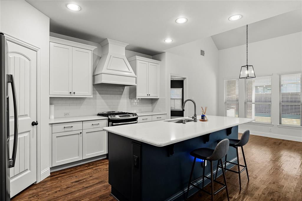 a kitchen with stainless steel appliances granite countertop a stove a sink dishwasher a refrigerator and white cabinets with wooden floor