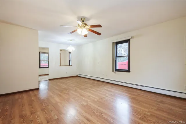 an empty room with wooden floor chandelier fan and windows