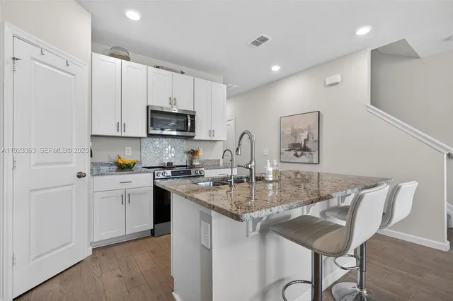 a kitchen with stainless steel appliances granite countertop a sink a stove a refrigerator cabinets and a dining table with wooden floor