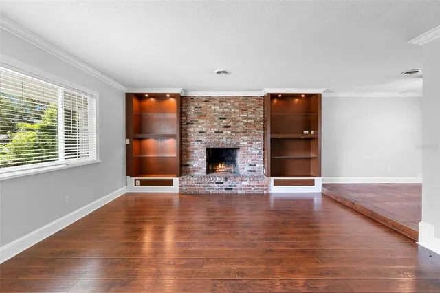 an empty room with wooden floor fireplace and windows