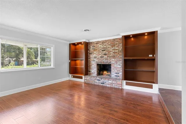 an empty room with wooden floor fireplace and windows