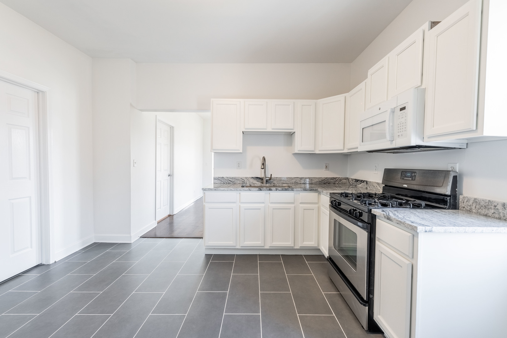 4140 West Maypole Avenue, Unit 2 Chicago, IL 60624 - Photo 10 of 24 a kitchen with stainless steel appliances granite countertop a stove a sink and a white refrigerator with white cabinets