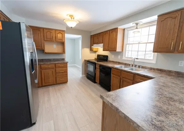 a kitchen with stainless steel appliances granite countertop wooden cabinets a sink dishwasher a stove and a refrigerator with wooden floor