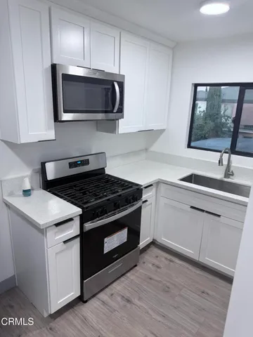 a kitchen with stainless steel appliances a sink dishwasher a microwave oven and white cabinets with wooden floor